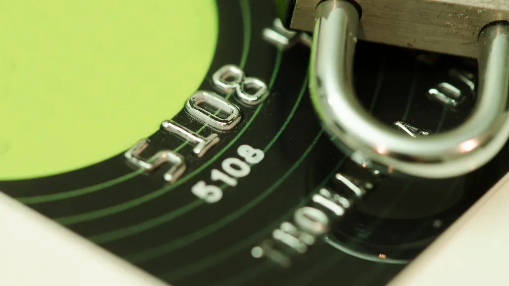 Close-up of a green and black credit card with embossed numbers 5108 and a silver padlock shackle resting over its surface.